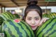 A young girl holding a large watermelon in front of her face.