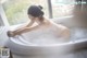 A woman in a white lingerie sitting in a bathtub.