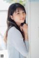 A young woman leaning against a wall with her hand on her chin.