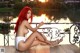 A woman with red hair sitting on a bench by the water.