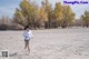 A woman running across a sandy field with trees in the background.